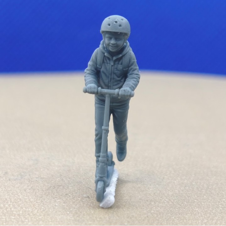 Enfant en trottinette avec casque et sac à dos à l’échelle 1:43, vu de face