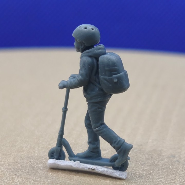 Enfant en trottinette avec casque et sac à dos à l’échelle 1:43, vue de trois quarts arrière