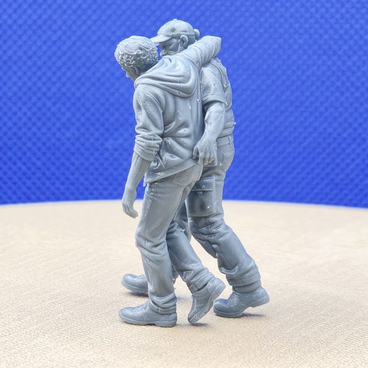 Homme blessé prenant appui sur un agent de sécurité, diorama 1:43 vu de dos
